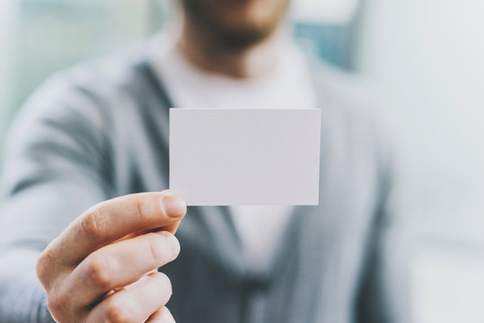 Closeup photo man wearing casual shirt and showing blank white business card. Blurred background. Ready for private information. Horizontal mockup