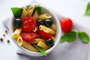 Cooked penne pasta with olives, fresh tomatoes and basil in white bowl