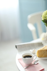 Cup of coffee with cake on white table in light interior