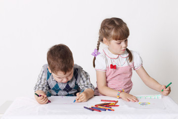 Little boy and girl draw with crayons sitting at table