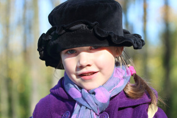 Little beautiful girl in black hat poses at sunny autumn day