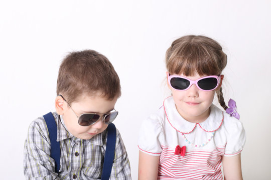 Little serious boy and smiling girl sit in sunglasses