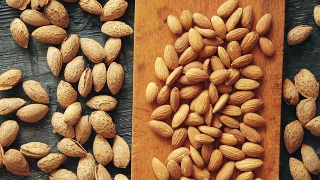 Almonds on wooden background. Peeled and unpeeled nuts on dark table. Dark and moody style. Magic moon and mistic light. Top view with rotation 360