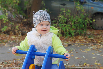 Little pretty girl in vest sits on wooden motorbike 