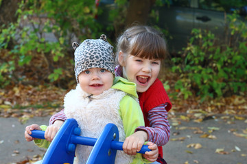 Girl in white vest and sister play on wooden motorbike playing 