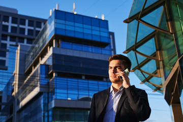 Man in suit talking on mobile phone against the building with a glass facade