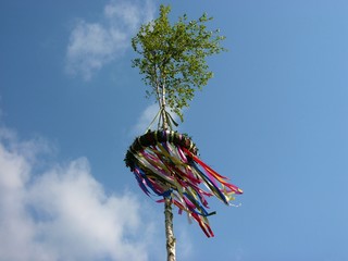 Bunte Bänder eines Maibaum oder Pfingstbaum im Wind vor blauem Himmel mit Wölkchen bei...