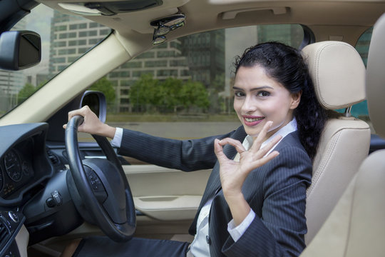 Indian woman driving a car and shows OK sign