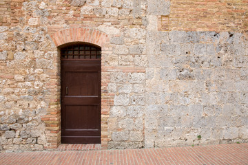 Fototapeta na wymiar Brown Door in a Medieval Tuscan Wall with Copy Space