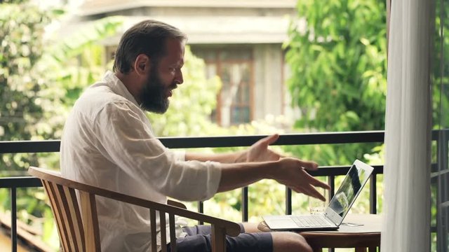 Angry, aggressive man destroying laptop sitting on terrace
