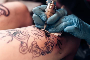 Foto op Aluminium Closeup tattoo artist fill circuit tattoo in a professional salon. Leg with a pattern and black paint. Master works in black sterile gloves.  © belyjmishka