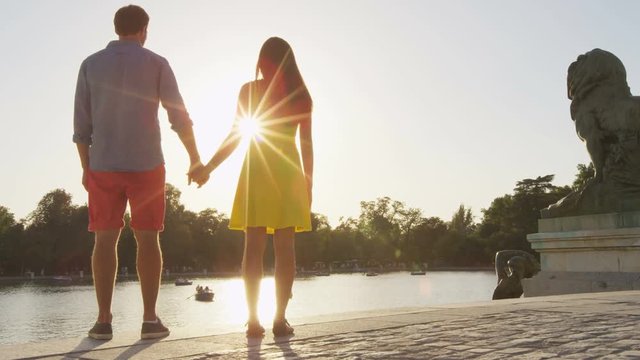 Romantic couple holding hands  in love enjoying view in park at sunset. Multicultural man and woman relaxing hand in hand on date in el Retiro in Madrid, Spain, Europe.