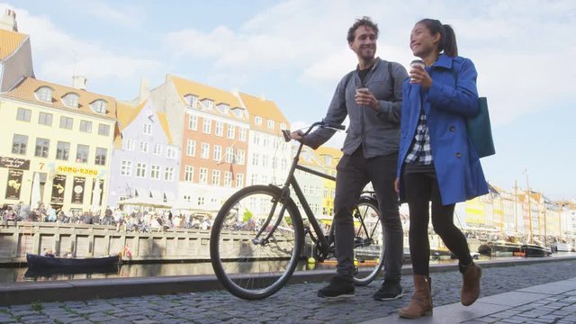 Copenhagen people. Couple walking in Nyhavn, old port. Famous tourist attraction destination in Denmark Young multiracial happy couple with bicycle bike and coffee. RED EPIC.