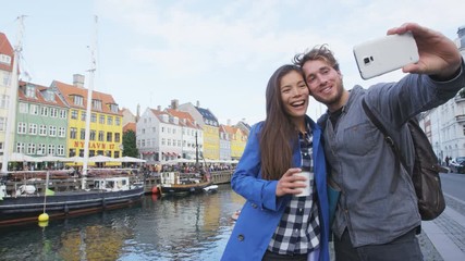 Copenhagen travel people taking friends selfie picture photos as souvenir with smart phone camera. Couple of tourists in the old port Nyhavn, famous Scandinavian attraction in Denmark, northern Europe - Powered by Adobe