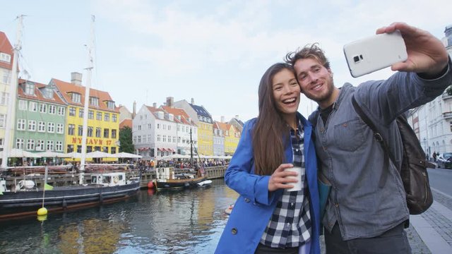 Copenhagen travel people taking friends selfie picture photos as souvenir with smart phone camera. Couple of tourists in the old port Nyhavn, famous Scandinavian attraction in Denmark, northern Europe
