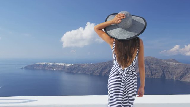 Vacation woman on luxury travel looking at view on Santorini famous Europe tourist destination. Elegant young lady living fancy jetset lifestyle wearing dress on luxury holidays. SLOW MOTION RED EPIC.