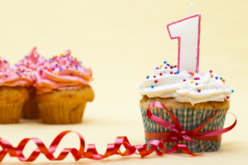 close-up image of a cupcake tied with ribbon white number 1 candle on top.