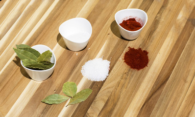 Spices in small dishes on a tray. Salt, red pepper and Bay leaf on a wooden background.