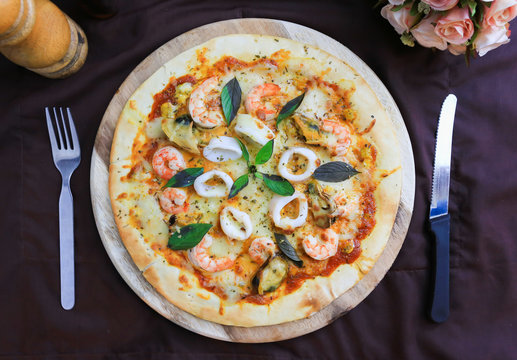 Delicious pizza with seafood on wooden stand, top view