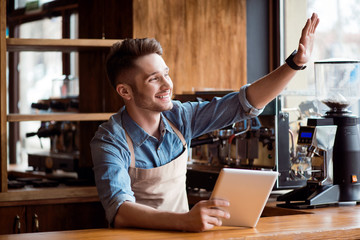 Pleasant barista using tablet  sitting at the counter  