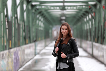 Obraz premium Beautiful brunette girl with leather jacket on a bridge