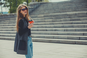 Beautiful girl standing on the street with coffee.