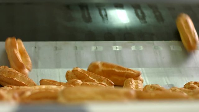 Pile of eclairs on conveyor. Eclair shells sliding down conveyor. High-quality dough for confectionery. First production step is complete.
