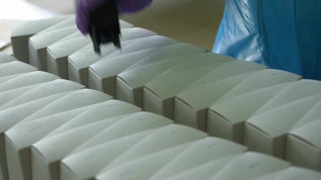 Hand putting stamp on boxes. White boxes with small stamp. Applying serial numbers on packages. New shipment is almost ready.
