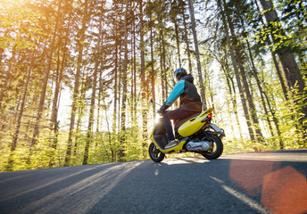 Man riding scooter on forest road.