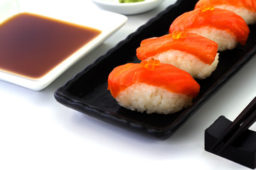 Salmon Sushi on the black plate on a white table.