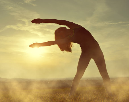 Silhouette of young woman stretching on a meadow at sunset