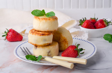 Fritters of cottage cheese with strawberries, sugar powder and mint on wooden background. Selective focus