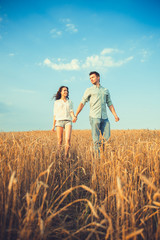 Naklejka na ściany i meble Young couple in love outdoor.Stunning sensual outdoor portrait of young stylish fashion couple posing in summer in field.Happy Smiling Couple in love.They are smiling and looking at each other