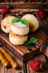 Fritters of cottage cheese with strawberries, sugar powder and mint on wooden background. Selective focus