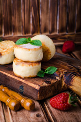 Fritters of cottage cheese with strawberries, sugar powder and mint on wooden background. Selective focus