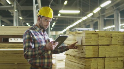 Worker counts wood stock using a tablet computer at a lumber factory warehouse. Shot on RED Cinema Camera.