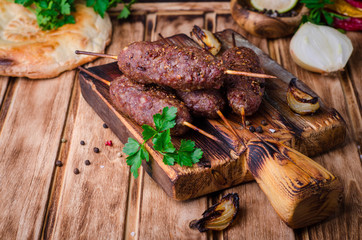 Roasted kebab skewer with spices on cutting board and wooden background. Selective focus