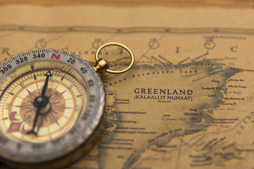 Fototapeta na wymiar Old compass on vintage map selective focus on Greenland