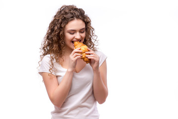 Curly woman eating a croissant on isolated background