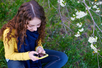 Beautiful young woman sitting on grass with a smartphone