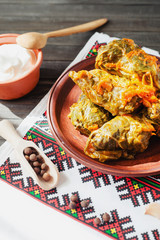 
National traditional Ukrainian and Russian cuisine , a dish called cabbage rolls , stewed rice with minced meat in cabbage leaves with sour cream , carrots and spices on a wooden background
