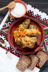 
National traditional Ukrainian and Russian cuisine , a dish called cabbage rolls , stewed rice with minced meat in cabbage leaves with sour cream , carrots and spices on a wooden background