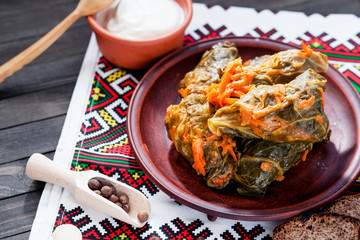 
National traditional Ukrainian and Russian cuisine , a dish called cabbage rolls , stewed rice with minced meat in cabbage leaves with sour cream , carrots and spices on a wooden background