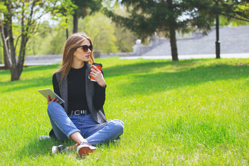 Girl sitting on the grass with coffee and tablet.