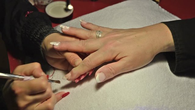A close-up of a hand of a woman in a nail salon receiving a manicure by a beautician. Woman getting nail manicure. Beautician paints nails to a customer.