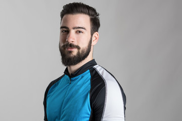 Portrait of bearded cyclist wearing jersey with copyspace looking at camera over gray studio background