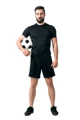 Fototapeten Smiling soccer or futsal player wearing black sportswear holding ball under his arm looking at camera. Full body length portrait isolated over white background. © sharplaninac