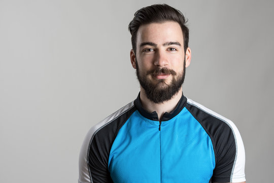Front view portrait of smiling happy cyclist wearing cycling jersey t-shirt over gray studio background.