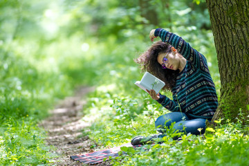 Lovely young brunette woman reading a book in a park, on a sunny day