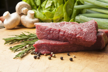 Fresh raw meat on wooden desk with mushrooms and rosemary